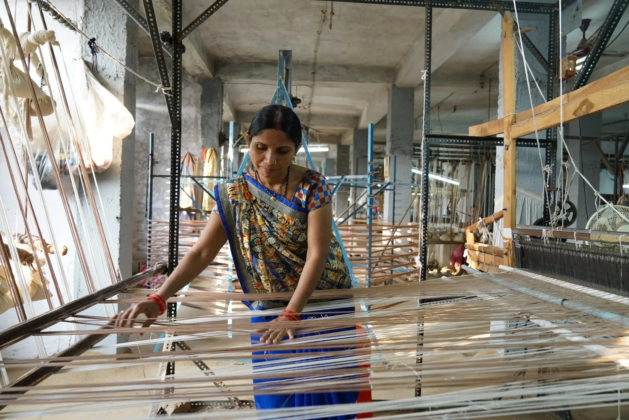 A weaver drawing warp threads across a handloom in a workshop